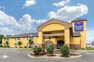 Un hotel Sleep Inn con fachada amarilla, una bandera estadounidense y un estacionamiento.