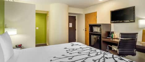 Habitación de hotel con cama, escritorio, silla, televisor y microondas.