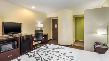 Habitación de hotel con cama, televisión, microondas, refrigerador pequeño, escritorio y lámpara.