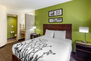 A hotel room with a large bed, a wooden headboard, a green accent wall, and two framed pictures.