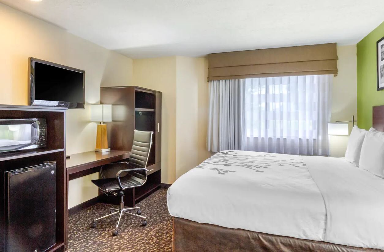 Ein Hotelzimmer mit Bett, Schreibtisch, Stuhl, Fernseher und Mikrowelle.