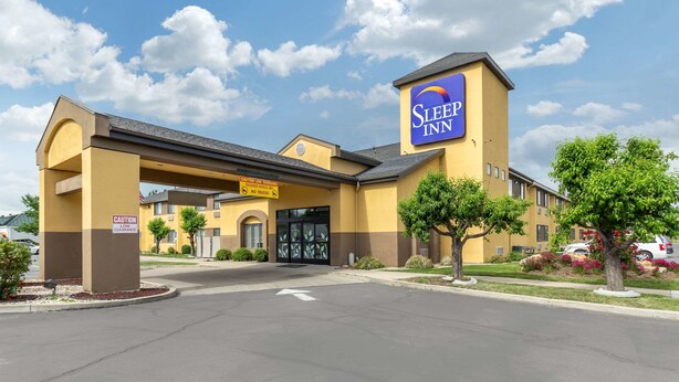 A Sleep Inn hotel with a yellow facade, a clear sky, and a parking lot.