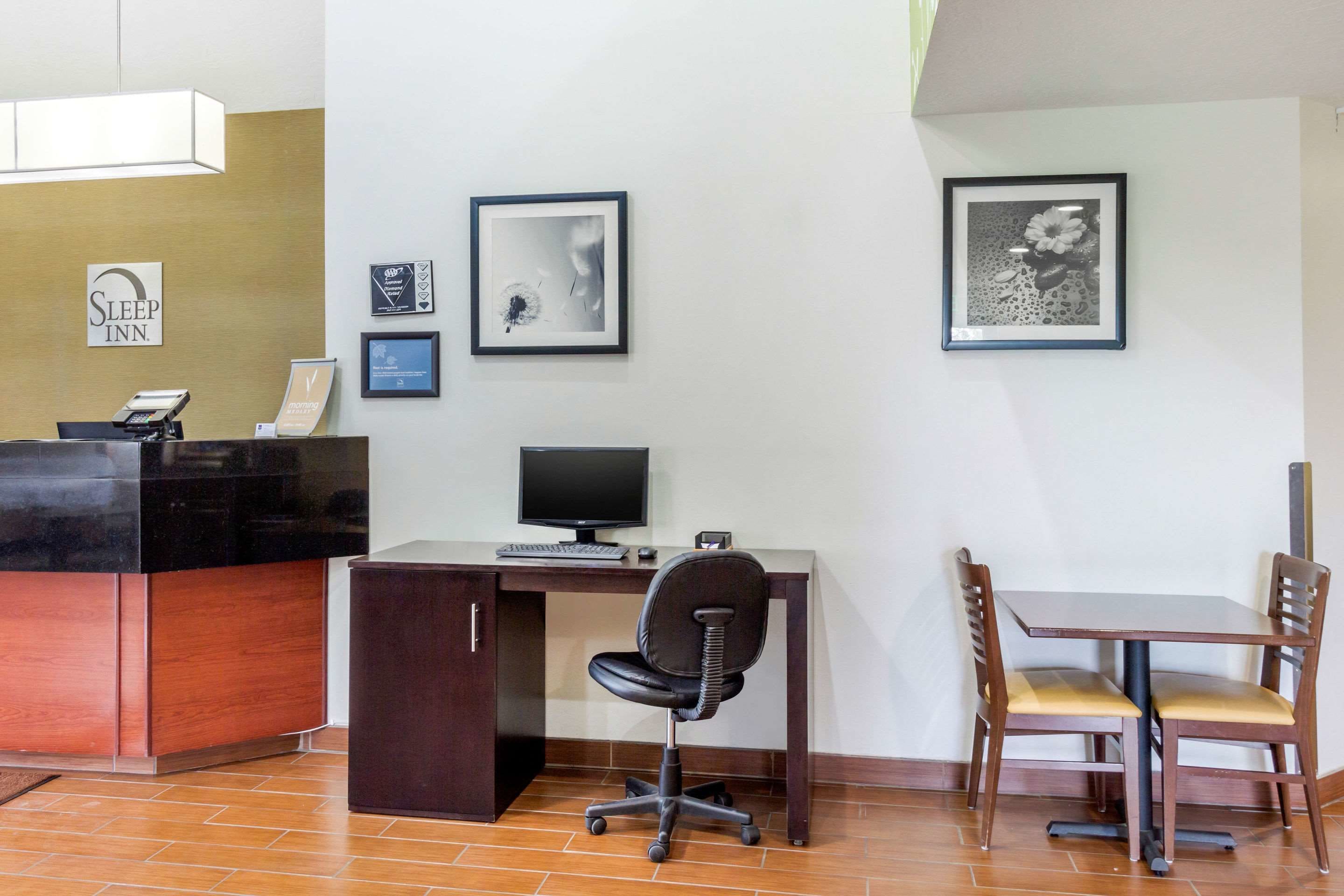 Un mostrador de recepción con una computadora, una silla y una mesa con sillas. Hay cuadros enmarcados en la pared.