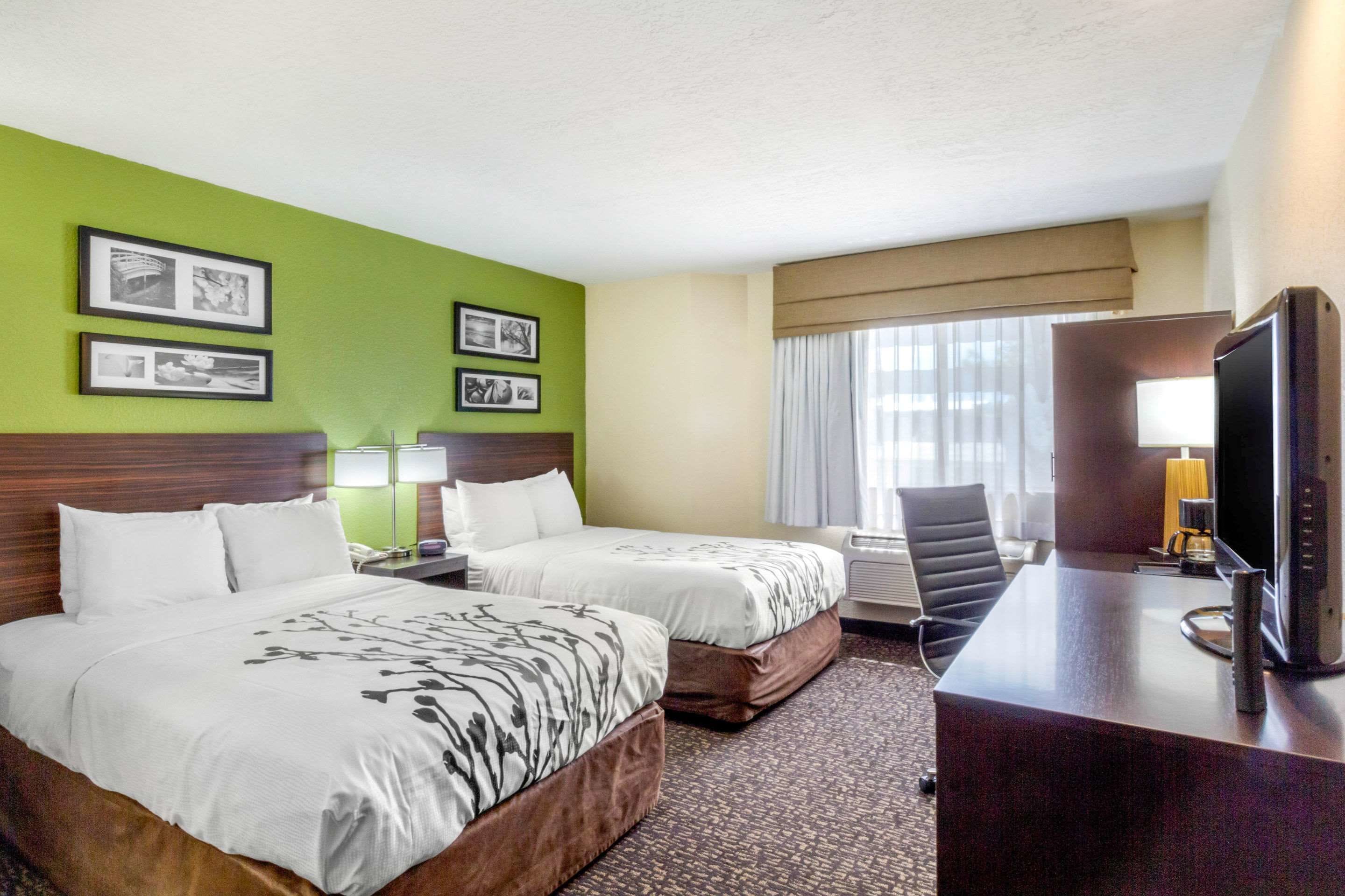 Ein Hotelzimmer mit zwei Betten, einem Schreibtisch mit Computer, einem Stuhl und einem Fernseher.