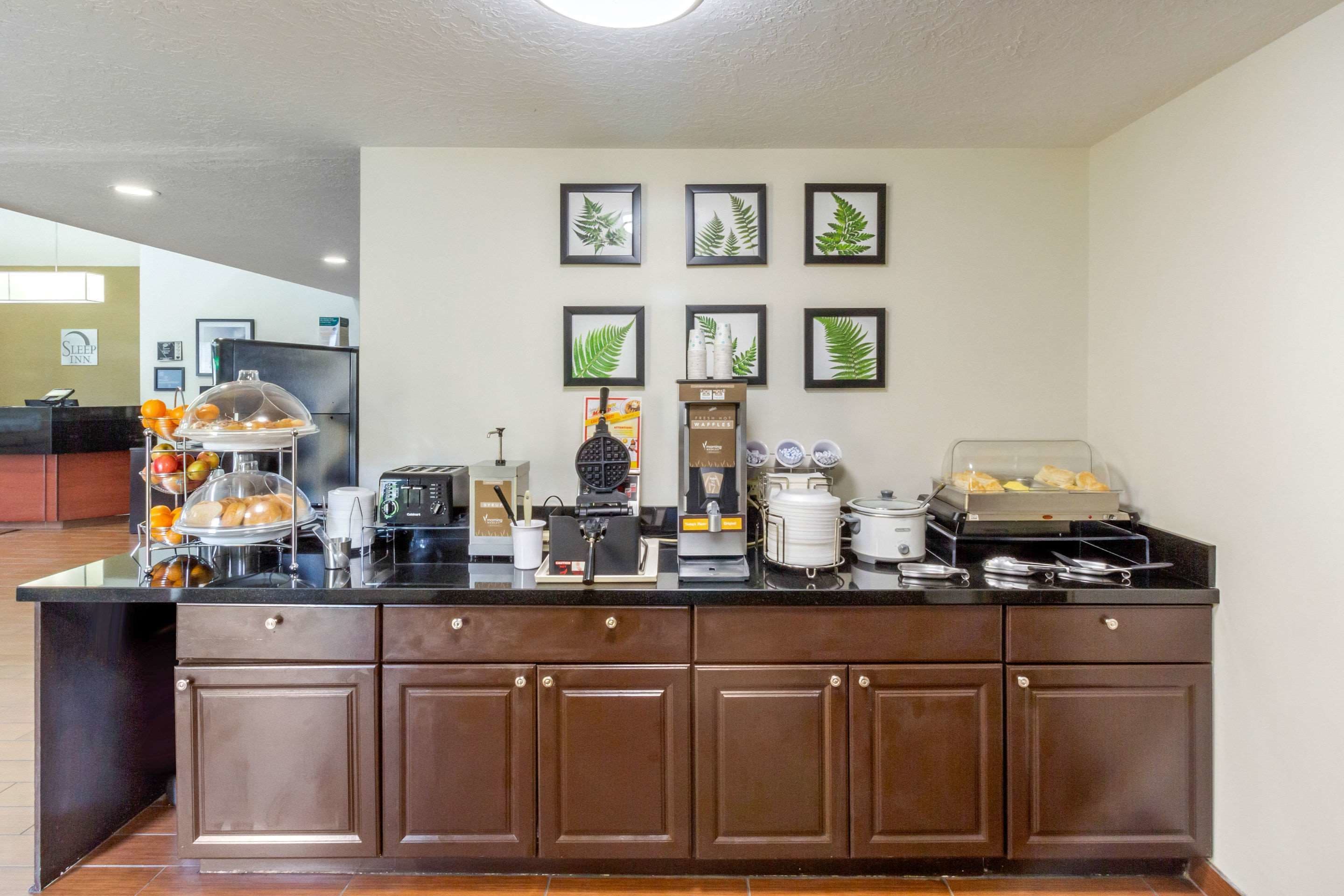 A hotel reception area with a counter, framed leaf artwork, a coffee machine, and a fruit display.