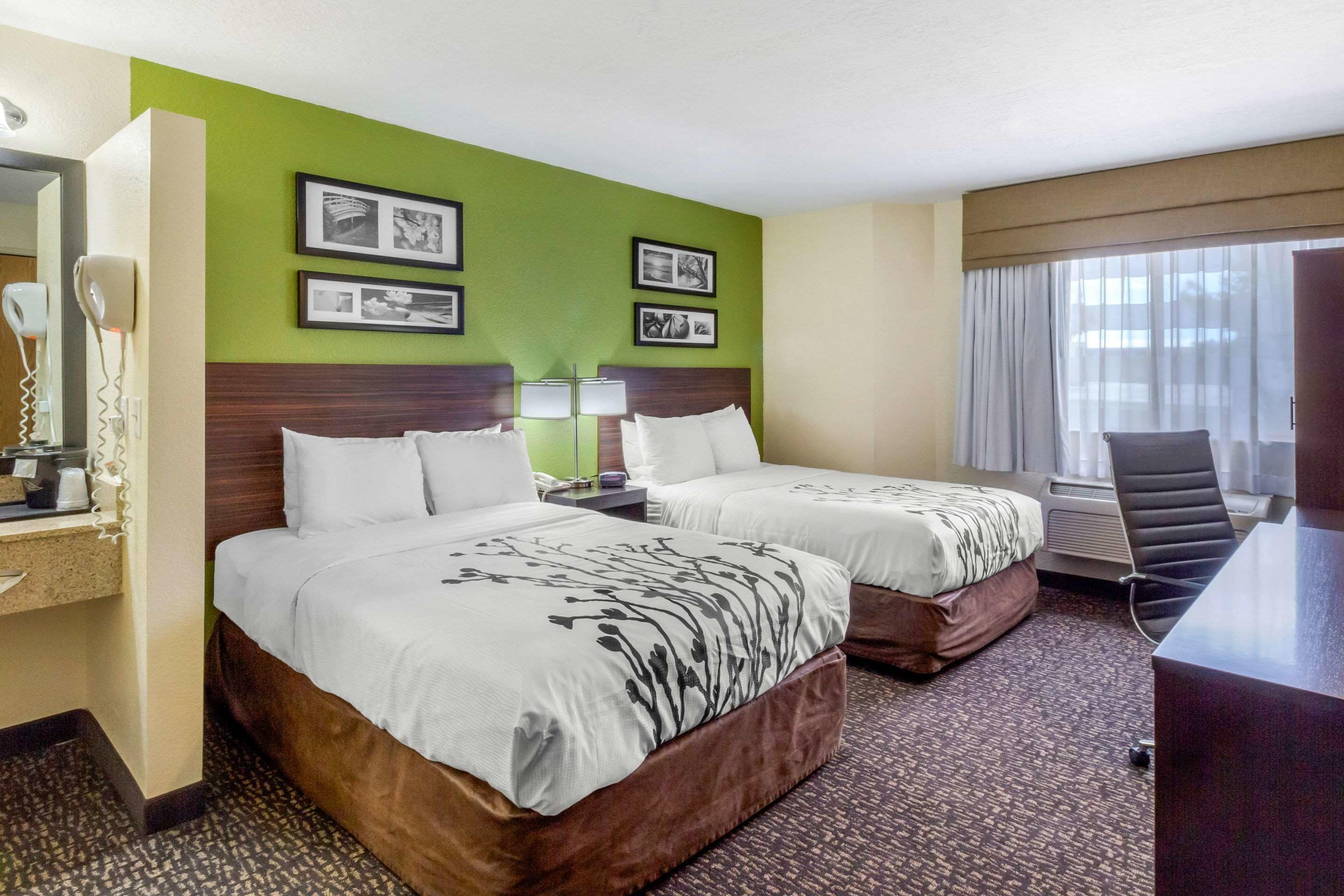 Een hotelkamer met twee bedden, een bureau, een stoel en een groot raam met gordijnen.