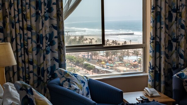 A hotel room with a large window offering a view of the beach and ocean. - Gooderson Tropicana Hotel (Durban)