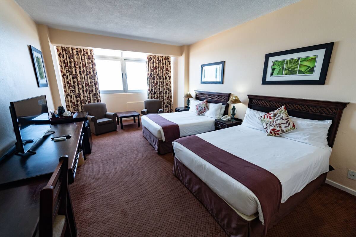 A hotel room with two beds, a desk, a chair, a TV, and a window with curtains.