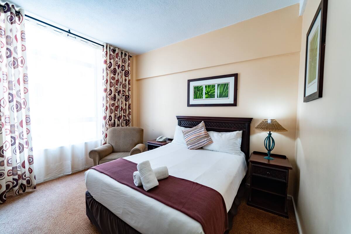 A hotel room with a bed, a chair, a nightstand, a lamp, and a framed picture on the wall.
