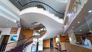 A hotel reception area with a curved staircase, a reception desk, and directional signs for rooms and facilities. - Gooderson Tropicana Hotel (Durban)