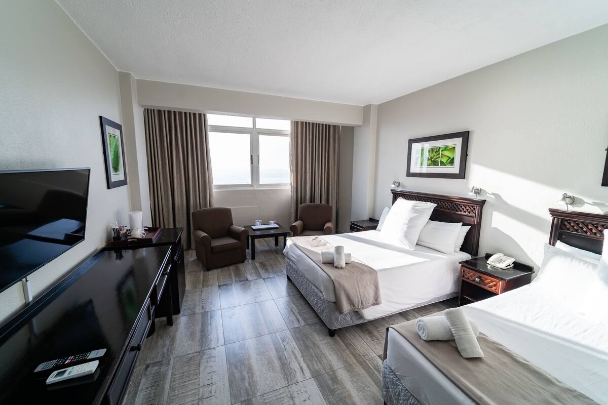 A hotel room with a bed, a TV, a desk, a chair, and a window with curtains.
