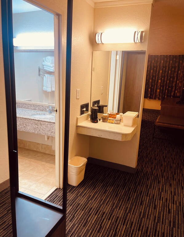 A hotel bathroom with a sink, mirror, and a coffee maker.