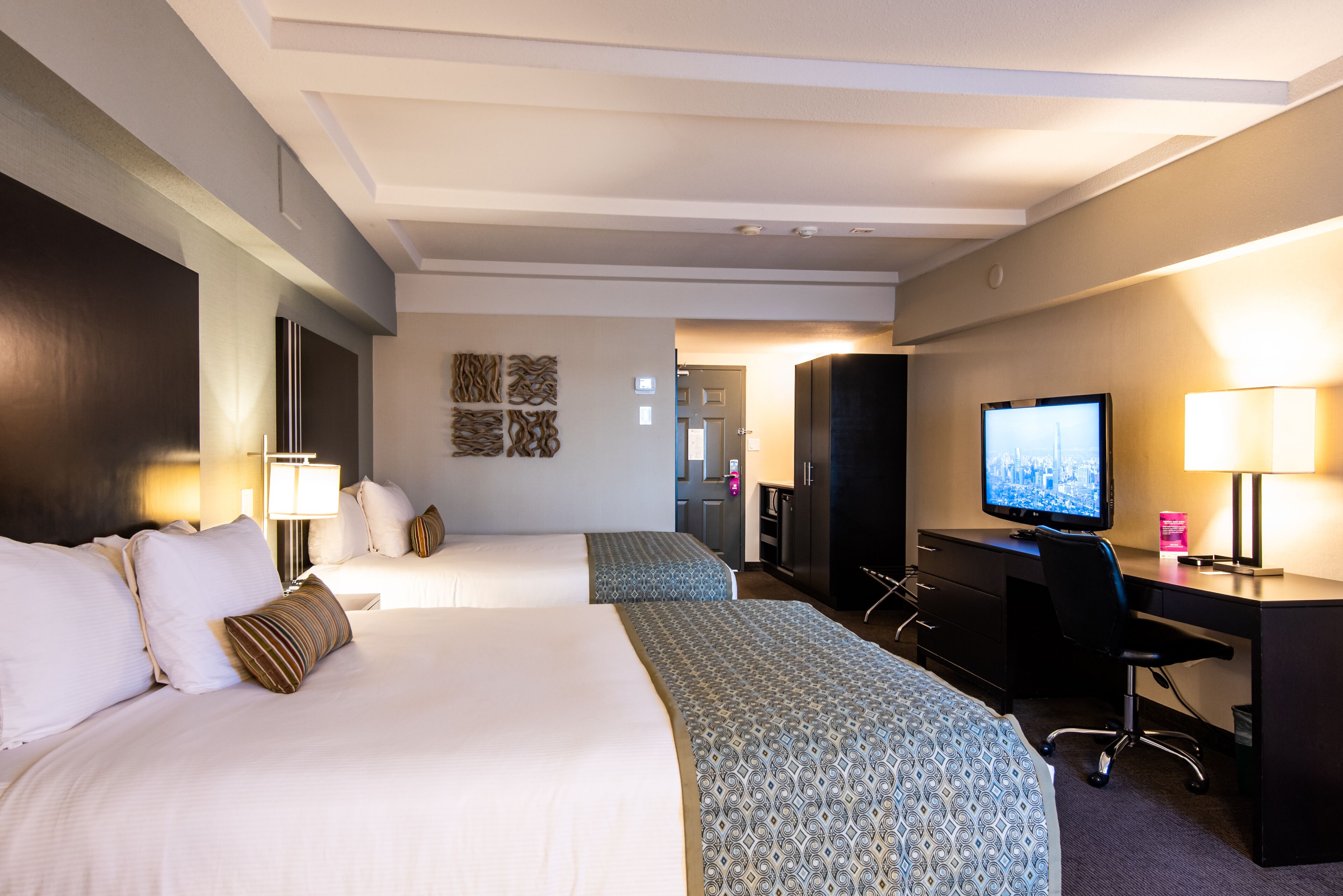 Una habitación de hotel con dos camas, un escritorio, un televisor y una obra de arte colgada en la pared.
