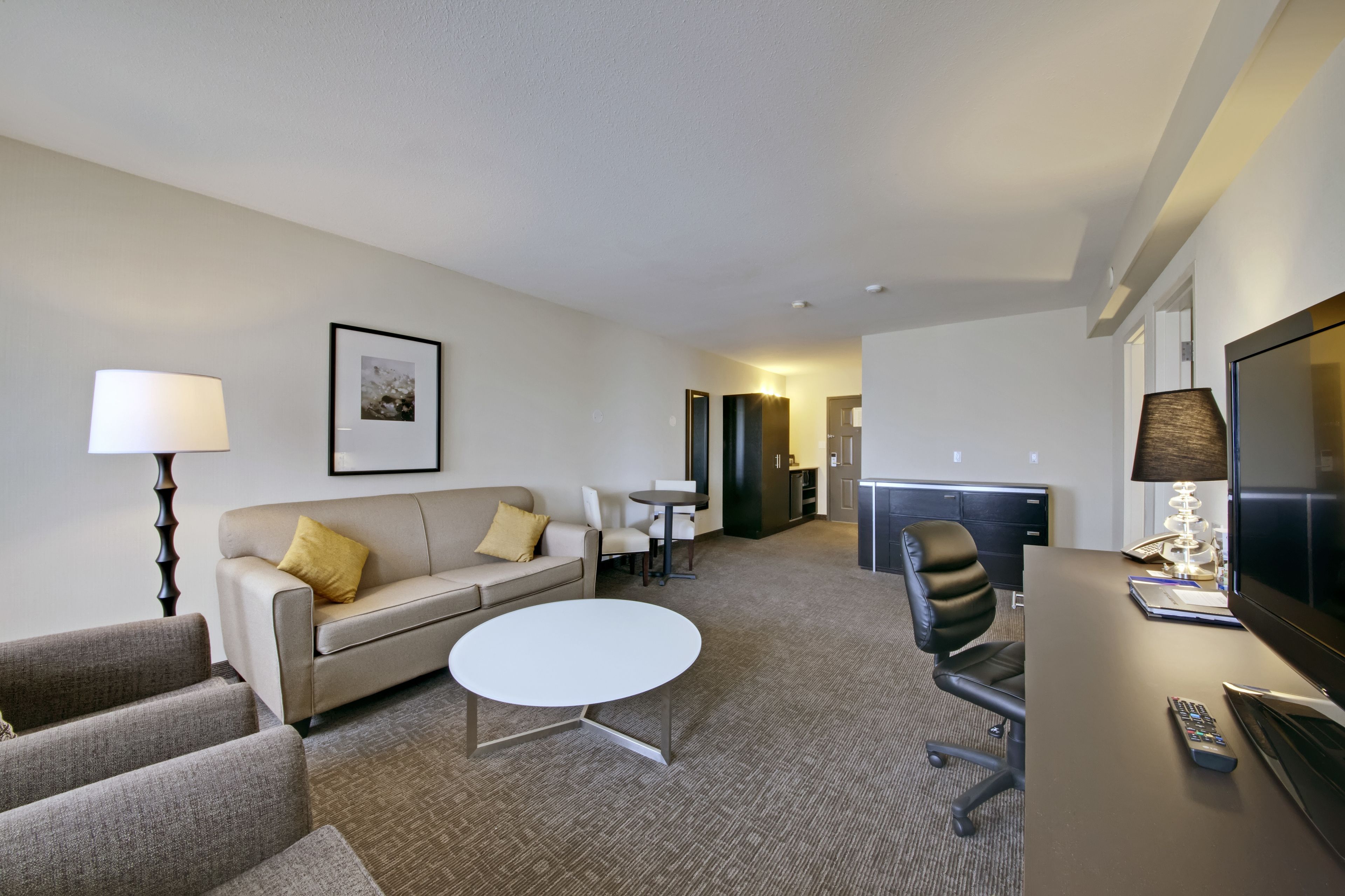Een hotelkamer met een bank, een rond bijzettafeltje, een televisie, een bureau en een stoel.