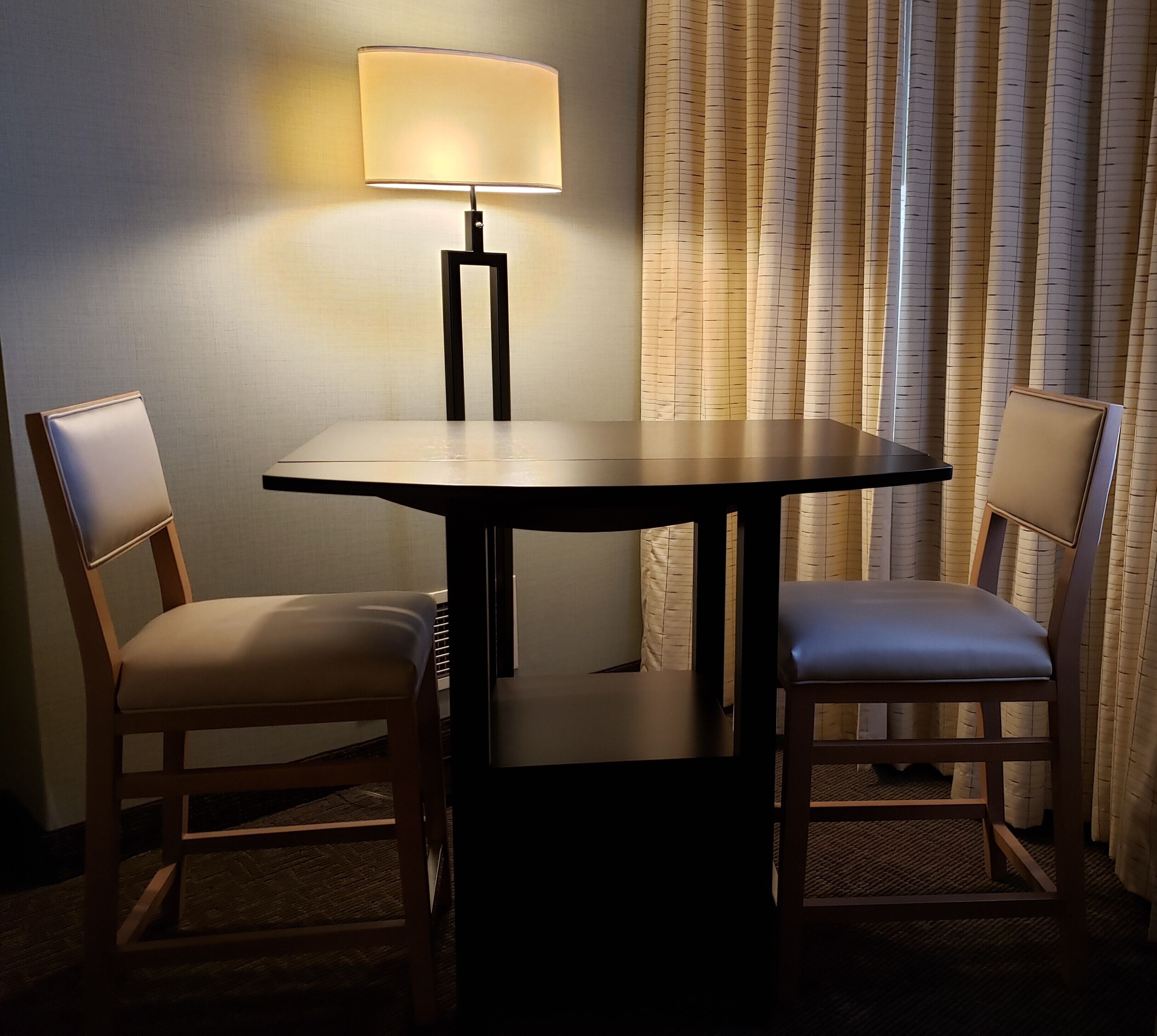 A hotel room with a round table, two chairs, a lamp, and a curtain.