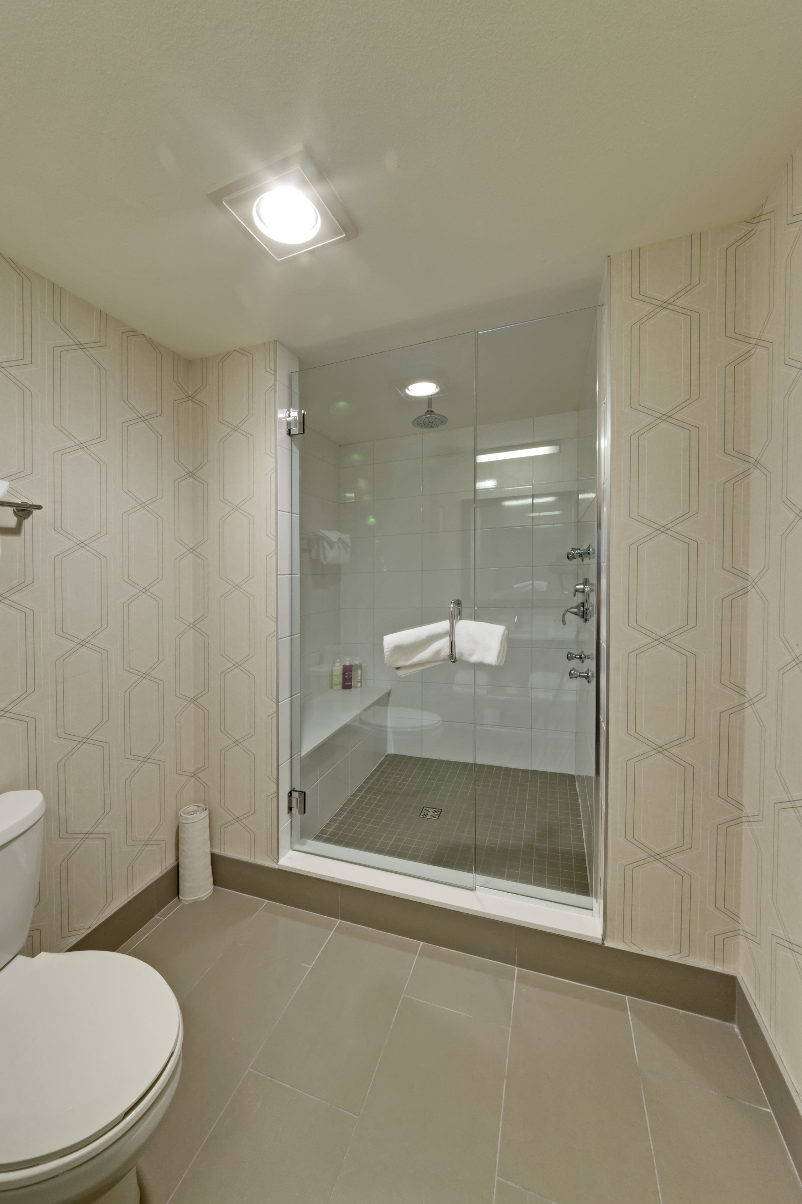 A modern bathroom with a glass-enclosed shower, a toilet, and patterned walls.