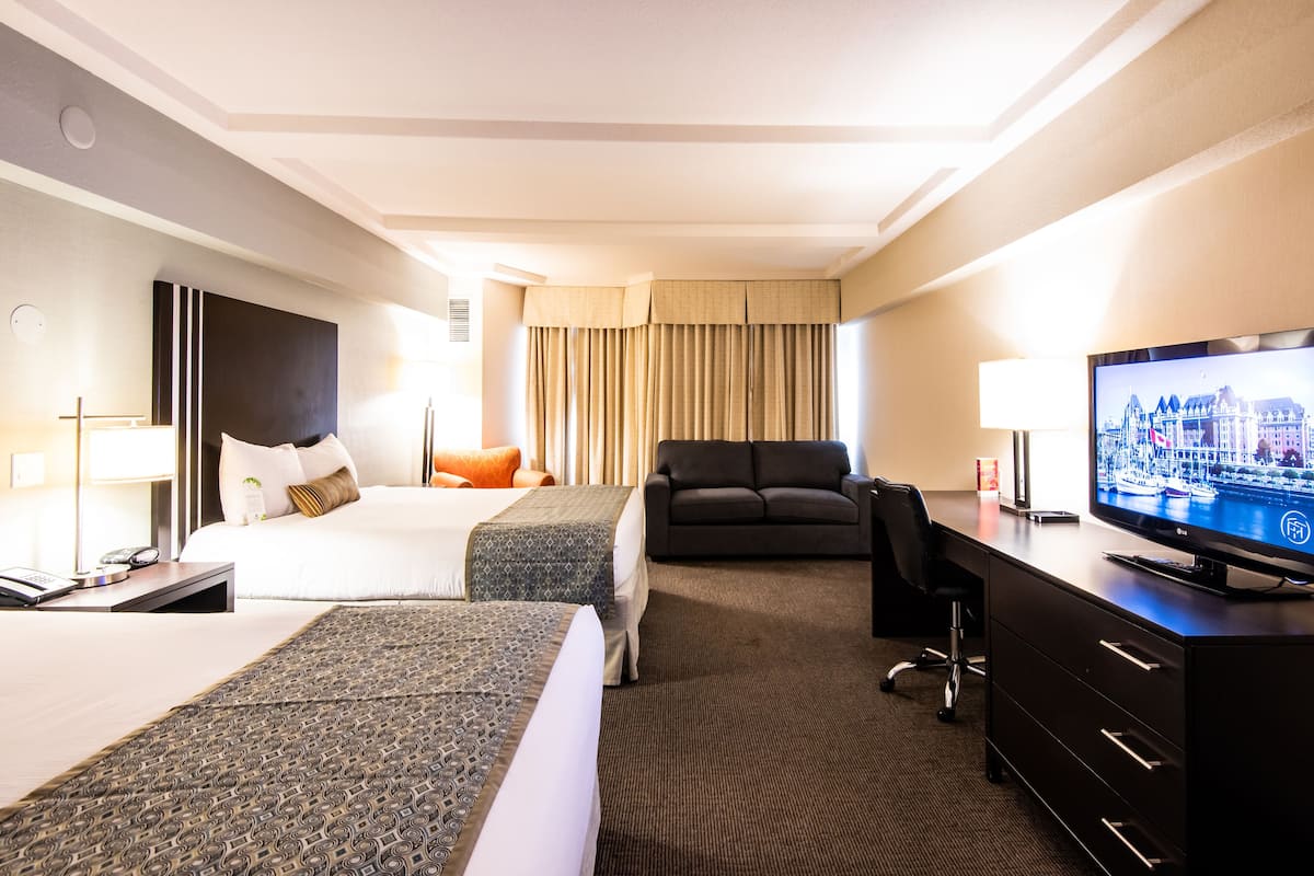 A hotel room with two beds, a desk, a television, and a sofa.