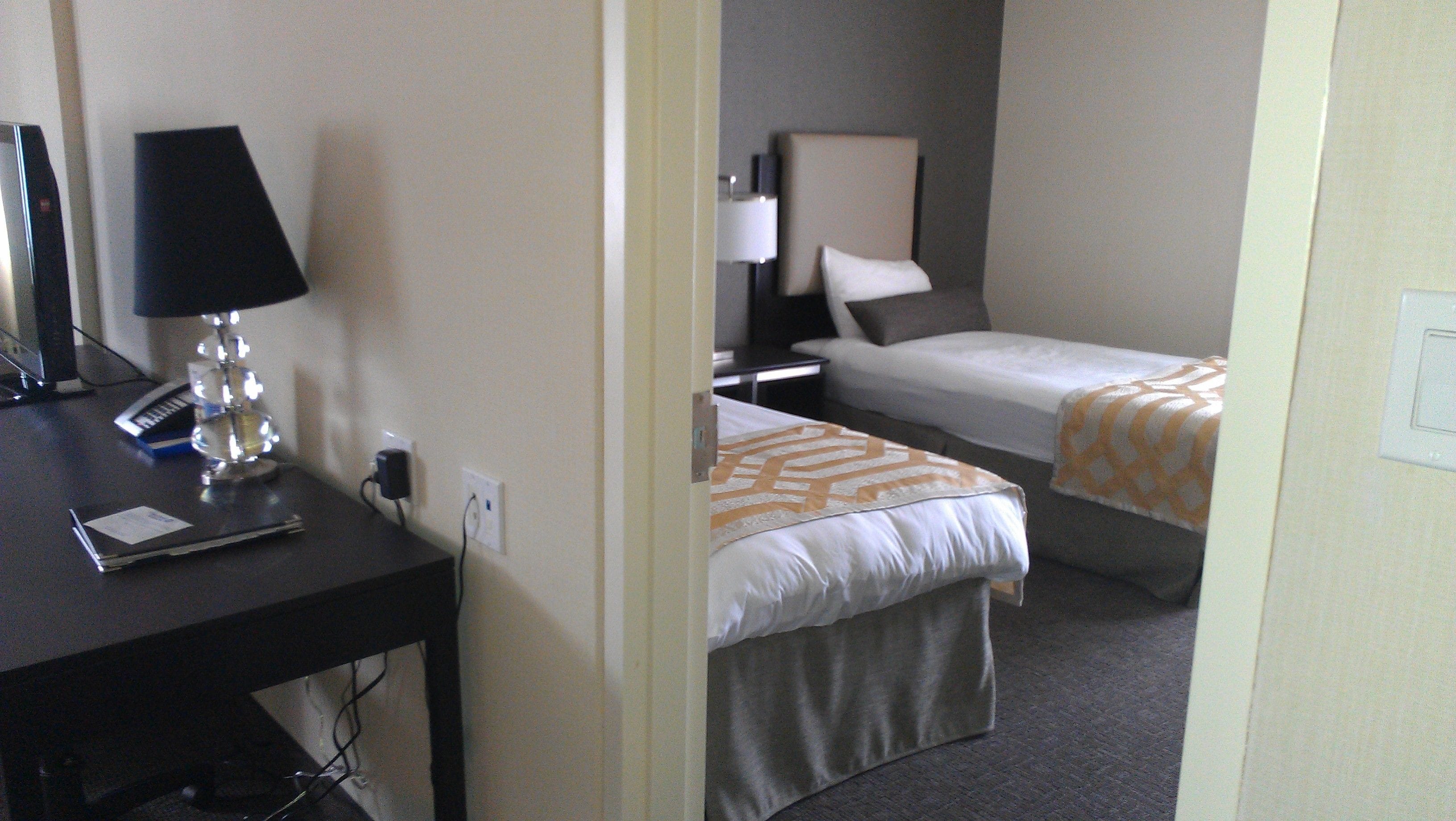 Ein Hotelzimmer mit zwei Einzelbetten, einem Schreibtisch mit Lampe, einem Telefon und einem Computer.