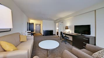 Moderni hotellihuone, jossa on sohva, pieni pyöreä pöytä, televisio, työpöytä ja tuoli.