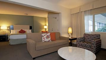 A hotel room with a bed, a sofa, a chair, a round table, and a window with curtains.