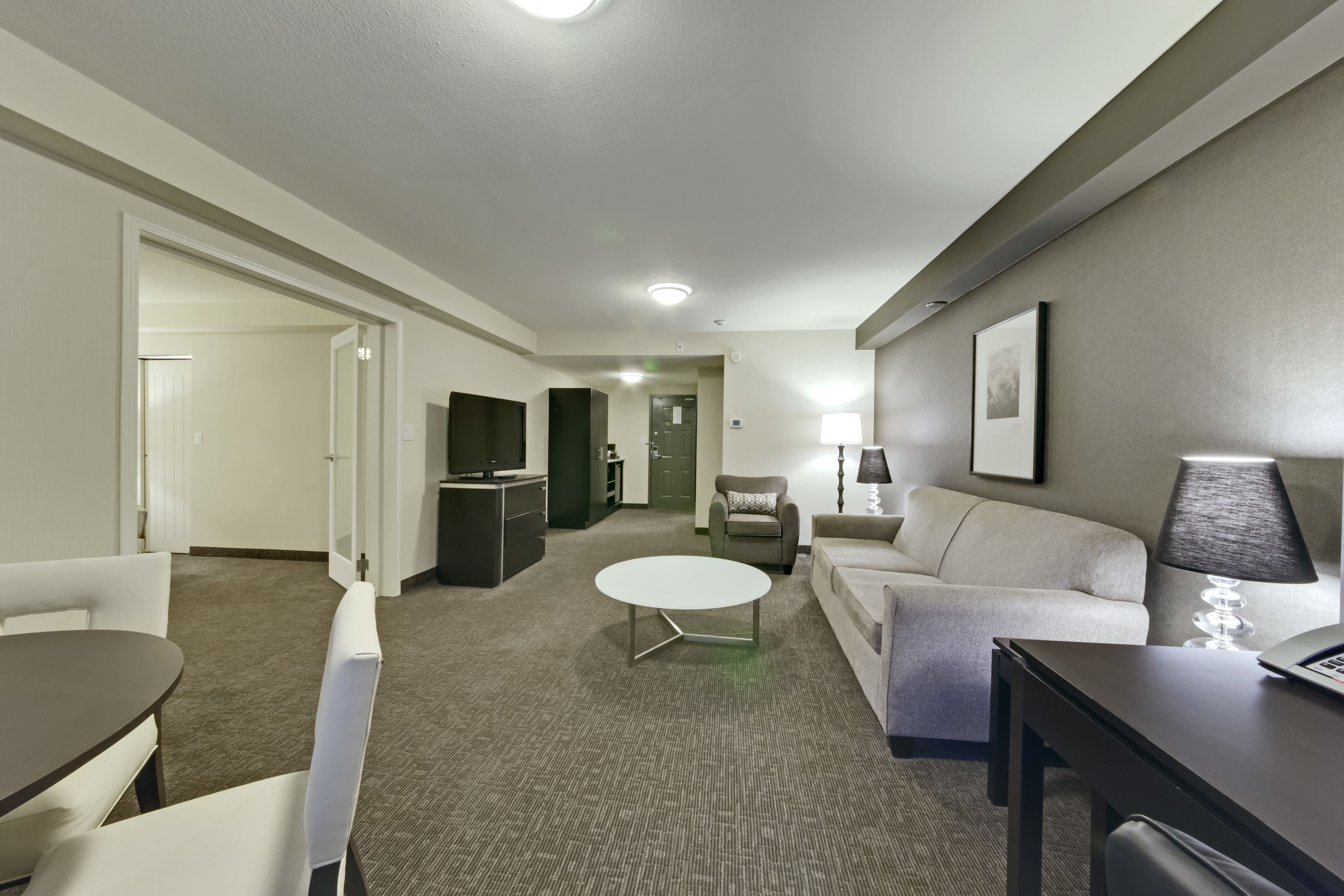 Ein modernes Hotelzimmer mit Essbereich, einer Couch, einem Couchtisch, einem Fernseher und einer Lampe.