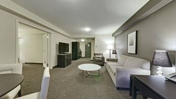 Ein modernes Hotelzimmer mit Essbereich, einer Couch, einem Couchtisch, einem Fernseher und einer Lampe.