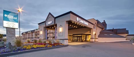 A hotel with a lobby entrance, outdoor pool, and a sign indicating amenities like indoor pool, hot tub, and WiFi.