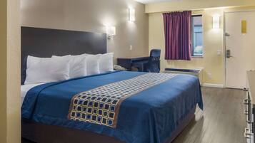 A hotel room with a large bed, a desk, a chair, and a window with curtains.