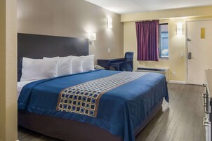 A hotel room with a large bed, a desk, a chair, and a window with curtains.