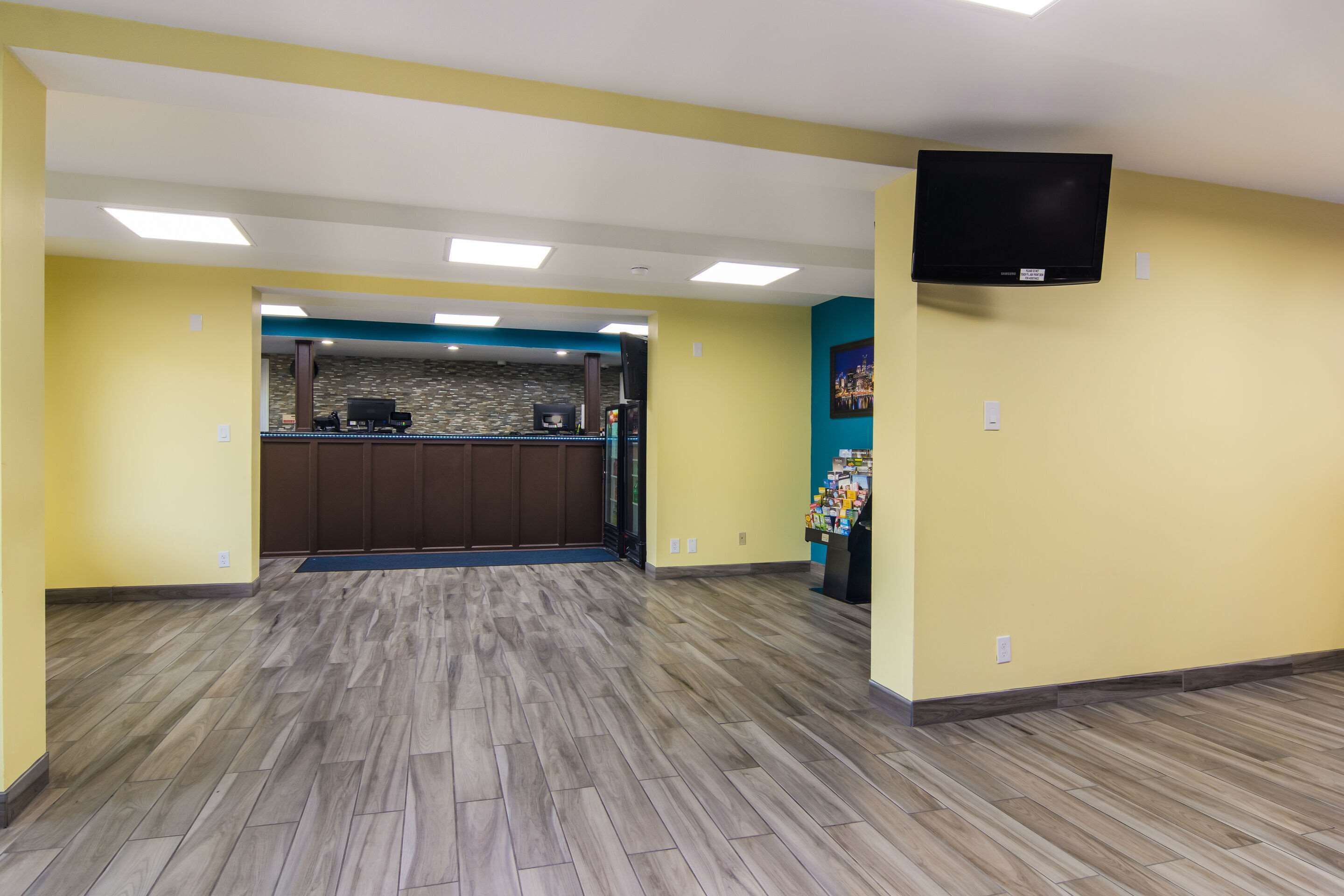 A hotel lobby with a reception desk, a flat-screen TV mounted on the wall, and a patterned floor.