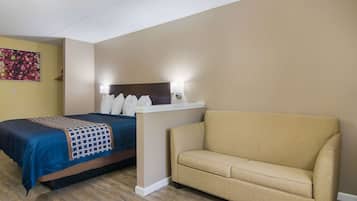 Habitación de hotel con cama, sofá beige y un cuadro floral en la pared.