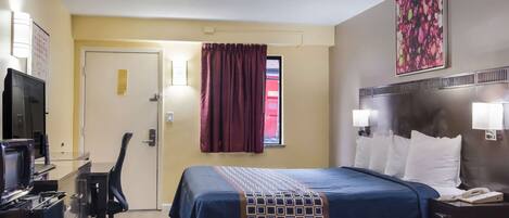 A hotel room with a bed, a desk with a computer, a chair, a TV, and a window with curtains.