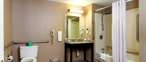 A bathroom with a toilet, sink, mirror, shower, and grab bars.