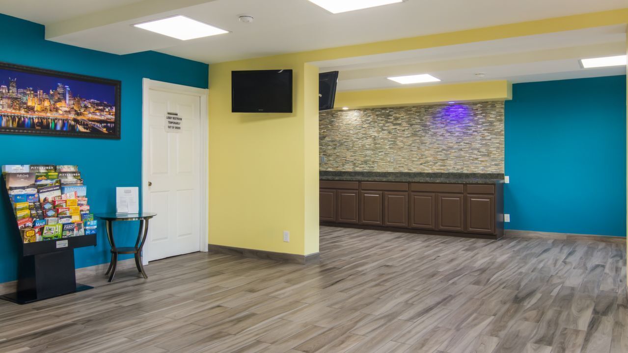 A room with a kitchen area, a door with a sign, and a wall-mounted TV.
