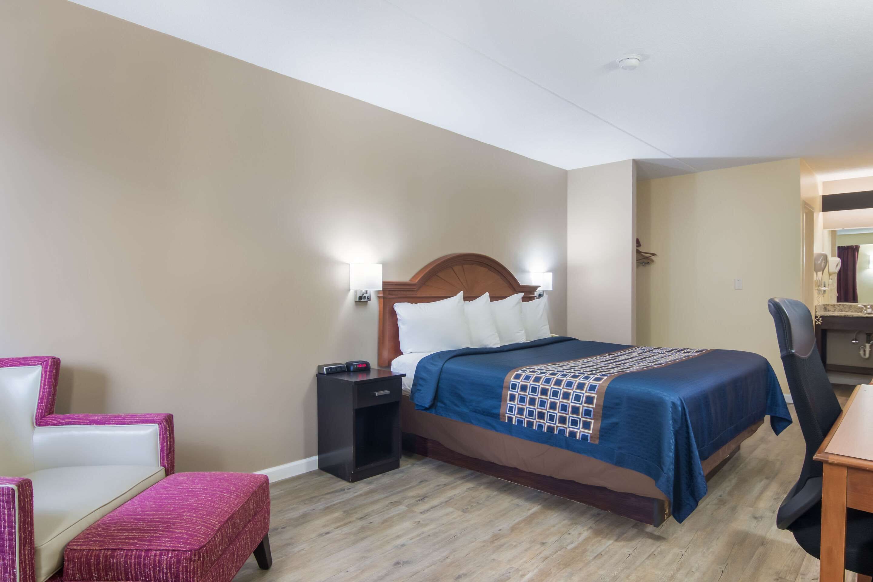 Habitación de hotel con cama, mesita de noche, silla y un pequeño escritorio con espejo.