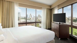 A hotel room with a large bed, a flat-screen TV, a wooden dresser, and a city view through large windows. - DoubleTree by Hilton Hotel Orlando Downtown (Orlando)