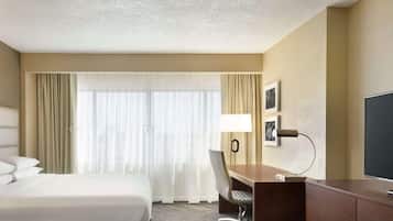 Habitación de hotel con cama, escritorio, silla, televisor y ventana con cortinas.