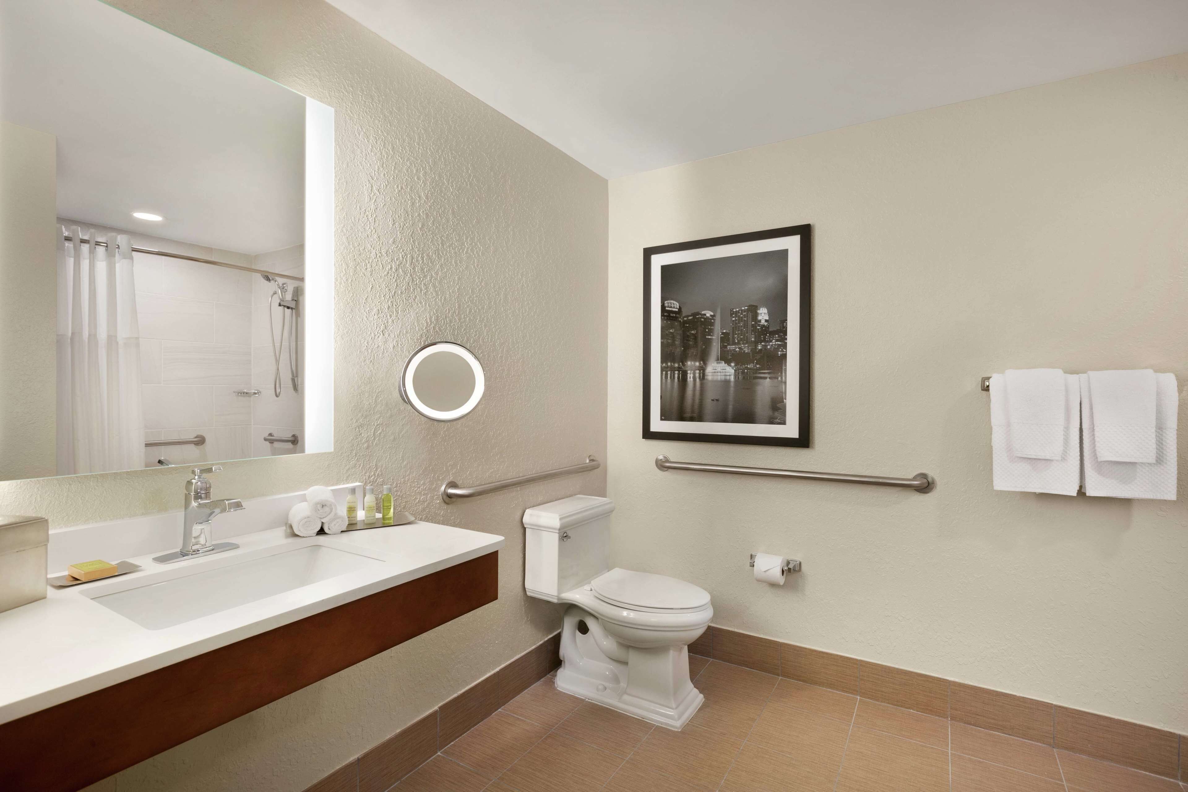 A modern bathroom with a large mirror, a sink, a toilet, and a framed picture on the wall.
