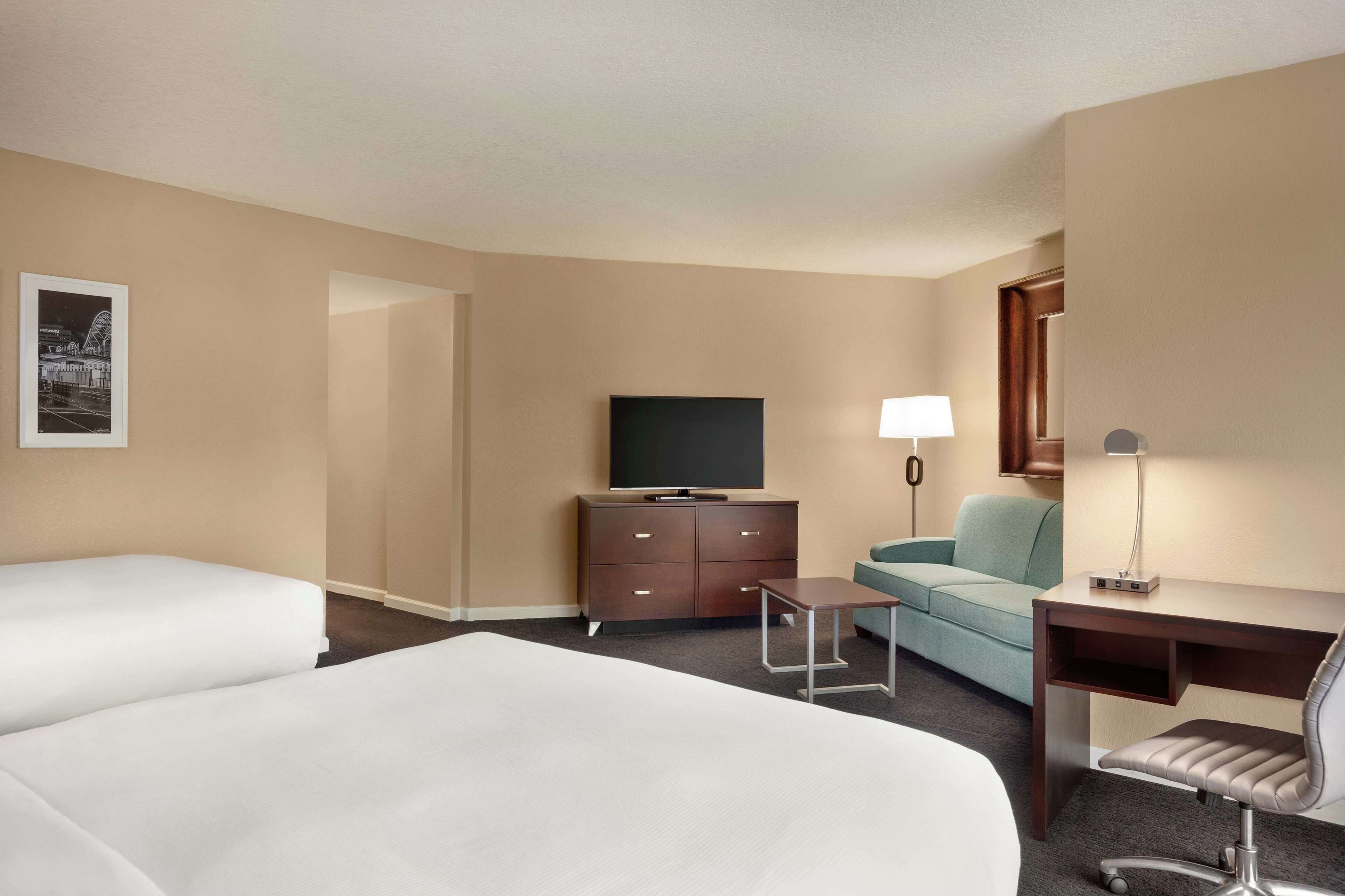 A hotel room with two beds, a desk with a chair, a television, a lamp, and a small table.