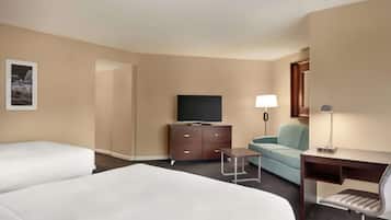 A hotel room with two beds, a desk with a chair, a television, a lamp, and a small table.