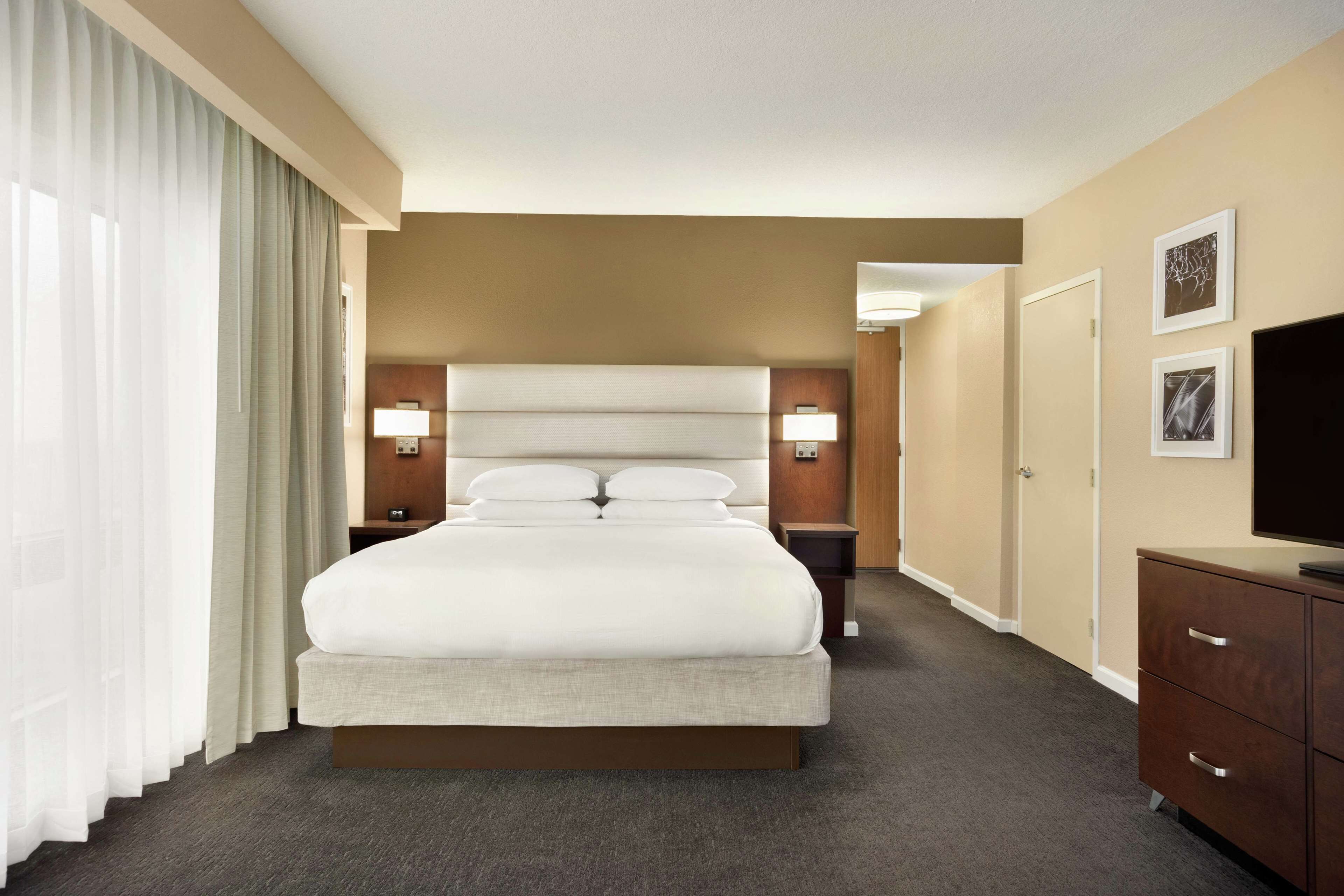A hotel room with a large bed, two bedside tables with lamps, a dresser, and a television.