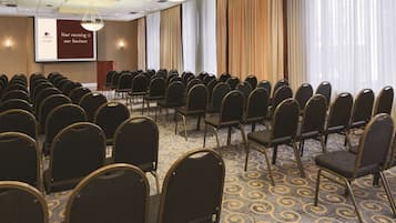 Une salle de conférence avec des rangées de chaises, un pupitre et un écran affichant un logo et du texte.