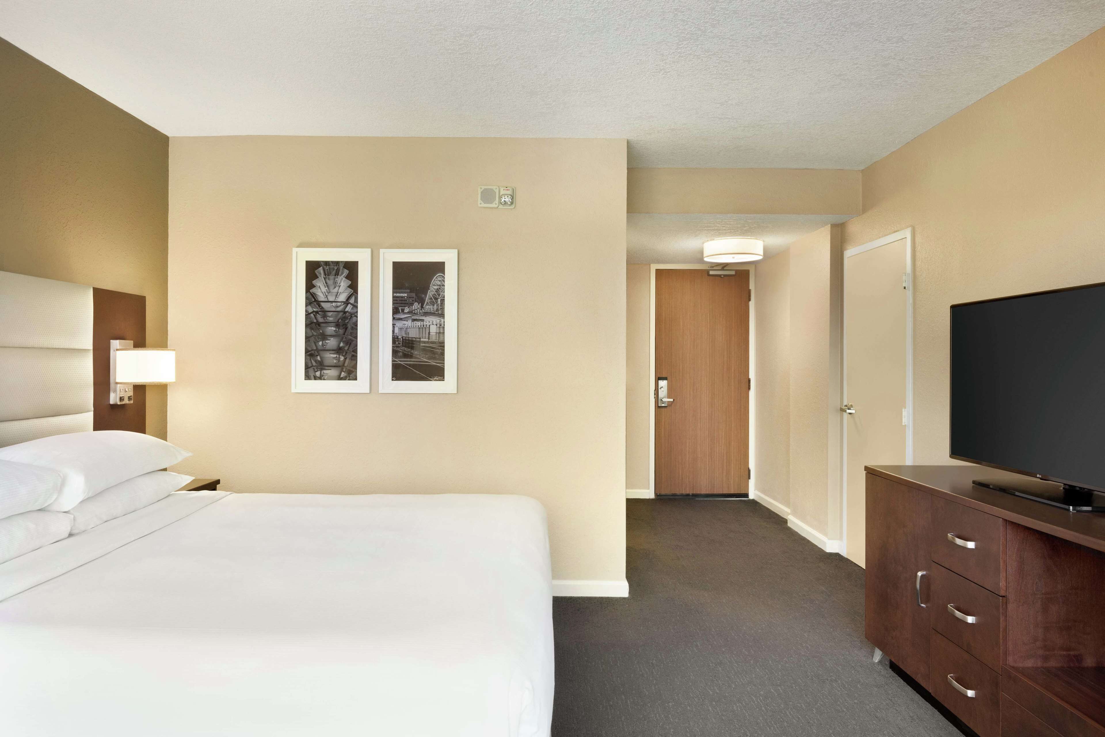 Une chambre d’hôtel avec un lit, un téléviseur posé sur une commode en bois et deux tableaux encadrés accrochés au mur.
