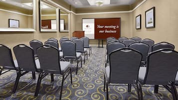 Un salón de conferencias con filas de sillas, un atril y una pantalla de presentación que muestra el texto 'Your meeting is our business'.