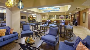 A spacious lobby with multiple seating areas, including sofas and chairs, a coffee table, and a bar area with a television. - DoubleTree by Hilton Hotel Orlando Downtown (Orlando)