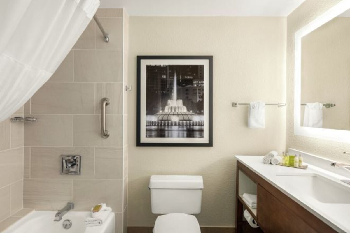 A modern bathroom with a bathtub, toilet, and sink. There is a framed picture of a fountain on the wall.