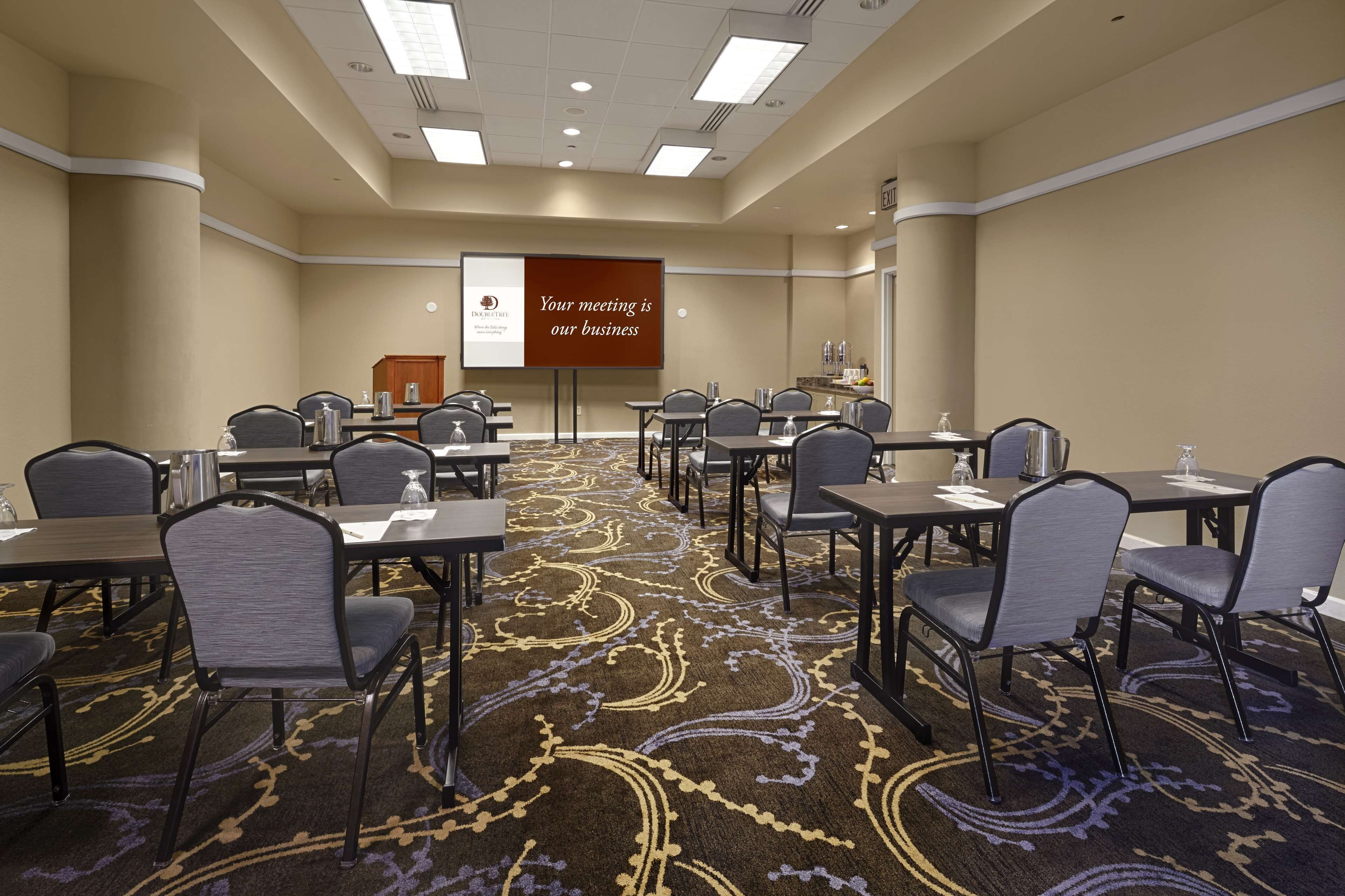 A conference room with a carpeted floor, multiple tables and chairs, a projector screen, and a podium.