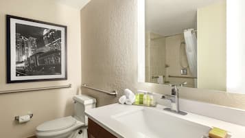 Une salle de bain moderne avec des toilettes, un lavabo et une douche. Un tableau encadré est accroché au mur et un miroir se trouve au-dessus du lavabo.
