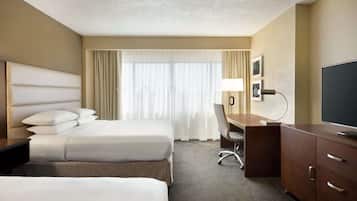 Une chambre d’hôtel avec deux lits, un bureau, une chaise, une télévision et une grande fenêtre avec des rideaux.