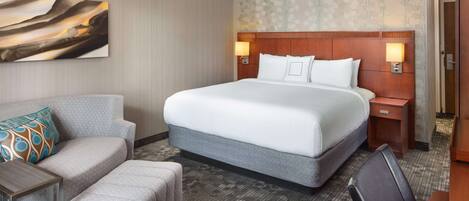 A hotel room with a large bed, a sofa, a small table, and a desk.